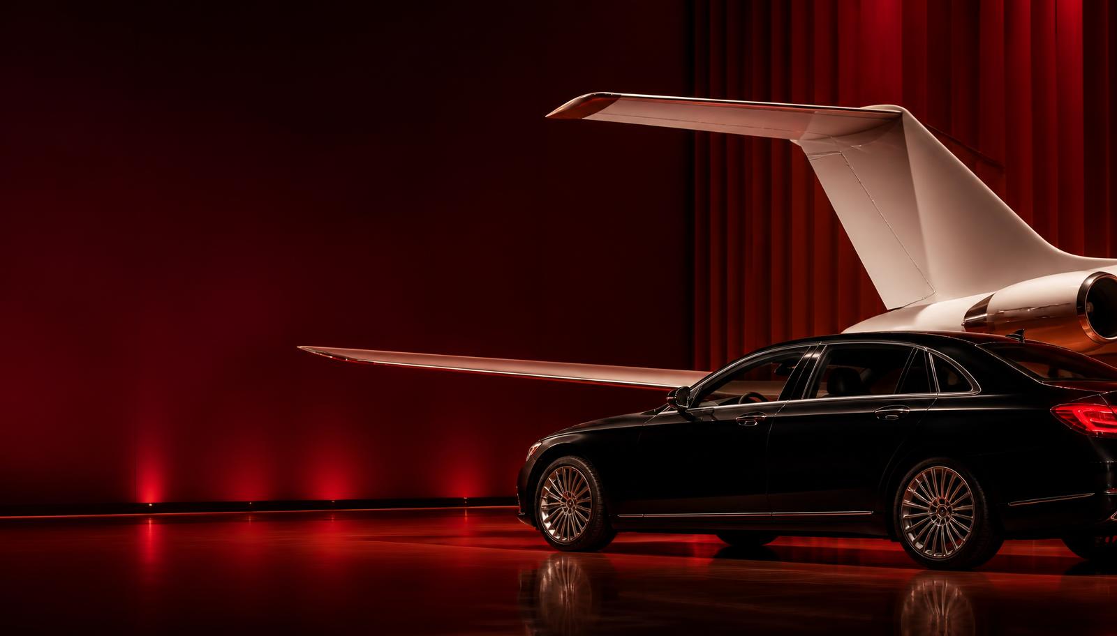 Luxury sedan beside a private aircraft in a dramatic red setting